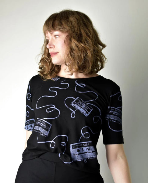 Woman wearing a black shirt with white graphic designs on a plain background