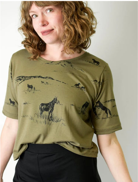 Person wearing a green t-shirt with black animal prints on a plain background